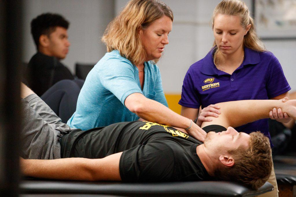 Two students and a professor working in the athletic training facility.